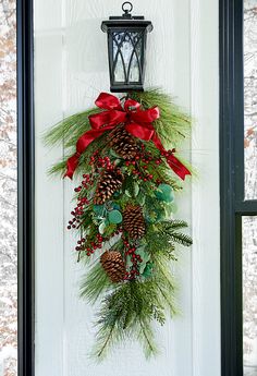 a christmas wreath hanging on the front door with red bows and pineconis,