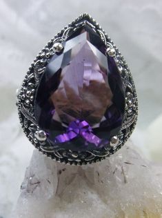 Natural Amethyst Gemstone Teardrop RingTear Vic Design#D28 Inspired by Victorian and Art Deco designs, this high-quality filigree ring is handcrafted in sterling silver. This teardrop ring is set with an 8.37 carat pear cut flawless natural purple amethyst gemstone. The gem is 16mm (~5/8") x 12mm (~1/2"). The gorgeous stones have lovely vibrant color. The inside of the band is marked 925 for sterling silver. Notice the beautiful filigree of the silver setting. This is a ring with beauty and grac Teardrop Amethyst Ring For Anniversary, Elegant Teardrop Amethyst Ring, Elegant Teardrop Amethyst Gemstone Ring, Formal Teardrop Amethyst Ring, Ornate Sterling Silver Amethyst Gemstone Ring, Ornate Sterling Silver Amethyst Ring, Sterling Silver Amethyst Ring With Intricate Design, Intricate Amethyst Ring In Sterling Silver, Intricate Design Amethyst Ring In Sterling Silver