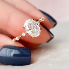 a woman's hand holding a ring with an oval shaped diamond in the middle