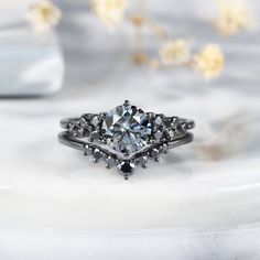 a white diamond ring sitting on top of a marble surface with flowers in the background