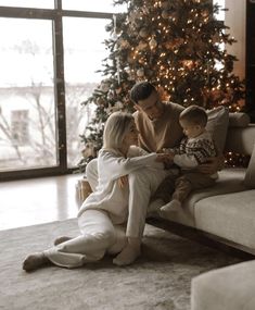 a man, woman and child sitting on a couch in front of a christmas tree