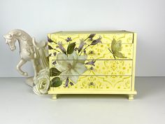 a yellow dresser with flowers painted on it and a white horse figurine next to it