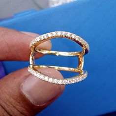 a person is holding a gold ring with diamonds on the inside and outside, in front of a blue box