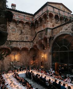 a large group of people sitting at tables in front of an old building with stone walls