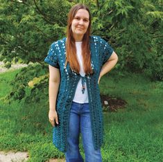 a woman standing in the grass wearing a blue crochet cardigan and jeans