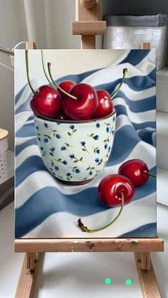 a painting of cherries in a bowl on an easel