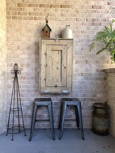 two metal stools sitting in front of a brick wall next to a potted plant