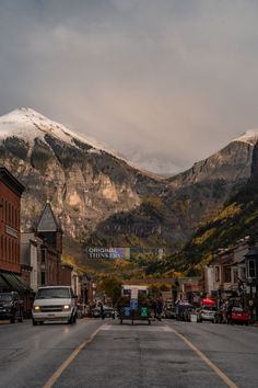 the mountains are covered in snow as cars drive down an empty street with buildings on both sides