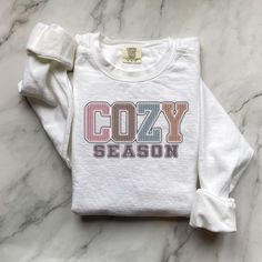 Fall Sweatshirt, Cozy Season Fall Sweatshirt, Cozy Season Merry Christmas, Christmas Sweatshirt, Winter Sweatshirt, Stay Home, Cozy Vibes Embrace the cozy vibes of fall and winter with our "Cozy Season" sweatshirt! Perfect for snuggling up at home, sipping hot cocoa, or celebrating the holidays in style. This soft and warm sweatshirt is your ultimate companion for chilly days and nights.  Available in festive "Merry Christmas" designs and classic fall styles. Luxurious comfort and style are what this unisex, garment-dyed sweatshirt is all about. It's made with 80% ring-spun cotton and 20% polyester and the fabric is 3-end garment-dyed, ring-spun, color-blast fleece with a 100% cotton face. Each sweatshirt comes with a relaxed fit, a rolled-forward shoulder, and a back neck patch.  .: 80% r Cozy Cotton T-shirt For Loungewear, Comfy Crew Neck Winter Tops, Long Sleeve T-shirt For Winter Loungewear, Comfortable Graphic Print Winter Tops, Comfortable Graphic Print Tops For Winter, Comfortable Winter Tops With Graphic Print, Cozy Sweatshirt For Fall Holiday, White Cotton Comfy Sweater, Cozy Sweatshirt For Holiday And Fall