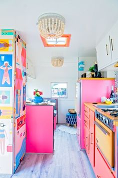 the kitchen is decorated in bright colors and has pink cabinets, white walls, and wood flooring