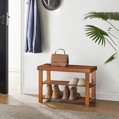 a wooden bench with shoes on it next to a coat rack and potted plant