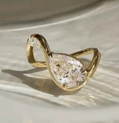 a yellow gold ring with a pear shaped diamond in the center, on a white surface