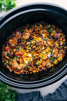 a crock pot filled with black beans, cheese and other toppings next to parsley