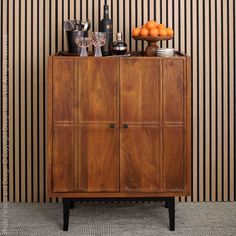 a wooden cabinet sitting in front of a wall with striped walls behind it and oranges on top