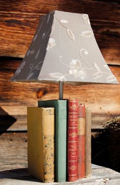 three books are stacked on top of each other in front of a lamp that is sitting on a piece of wood