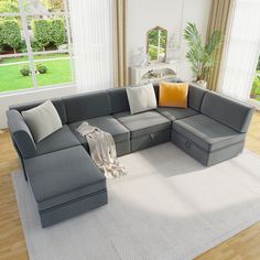 a living room with a large gray sectional couch and pillows on the floor next to a white rug