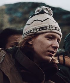 a woman wearing a hat standing next to other people in winter clothing and holding ski poles