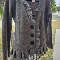 a gray jacket with ruffles on the front and back, hanging from a wire rack