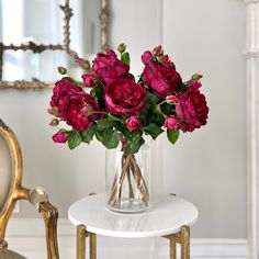 a vase filled with pink flowers sitting on top of a table next to a chair