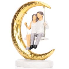 a figurine of two people sitting on a swing in the shape of a crescent