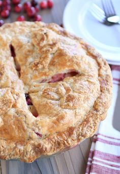 a close up of a pie on a table with cranberries in the background