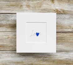 a blue heart is in the middle of a white box frame on a wooden surface