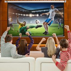 four people sitting in front of a large screen tv watching soccer on the television set