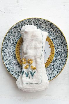 a plate with a napkin and some yellow flowers on it next to a white wall