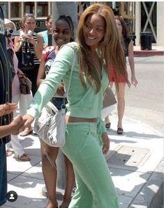 a woman is standing on the sidewalk with her hands in her pockets and smiling at someone