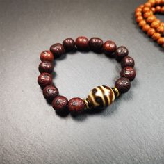 This unique Dalo Dzi bracelet combines the mysterious and unique qualities of the tiger tooth dalo dzi and 15 old bodhi seed beads,giving it a distinct feel.It is brown in color and has a circumference of approximately 7 inches, suitable for most wrist sizes.This bracelet can be worn not only as a fashionable accessory but also holds cultural and religious significance.Dzi beads are precious jewelry from Tibetan culture which are believed to possess the power of bringing good fortune to the owne Spiritual Brown Beaded Bracelets, Unique Hand-strung Brown Beaded Bracelets, Brown Wooden Beads For Bracelets, Spiritual Brown Bracelets With Wooden Beads, Spiritual Brown Bracelet For Meditation, Brown Spiritual Bracelets For Meditation, Brown Wooden Beaded Bracelet, Traditional Brown Beaded Bracelet With Polished Beads, Meditation Brown Bracelet With Polished Beads