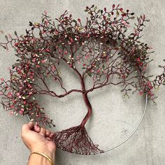 a hand holding a wire tree sculpture with red berries on it's branches and green leaves