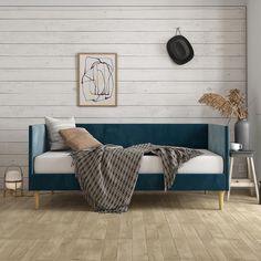 a living room with white walls and wood flooring is pictured in this image, the couch has a blanket draped over it