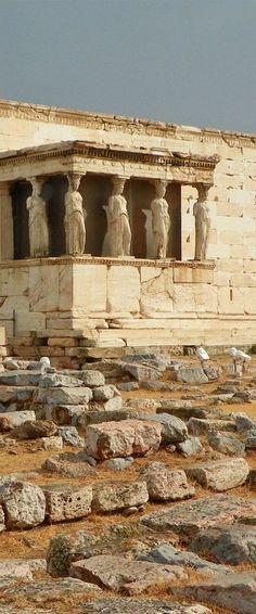 an ancient building with statues on the side and rocks in the foreground, against a blue sky