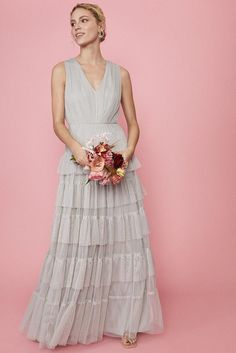 a woman in a long dress holding a flower bouquet and posing for the camera on a pink background