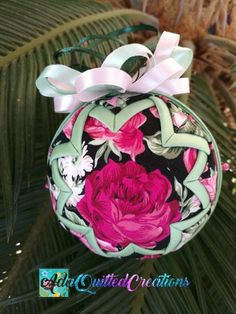 an ornament hanging from a palm tree with pink flowers and leaves on it