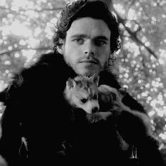 a man in a fur coat holding a small animal and looking at the camera with an intense look on his face