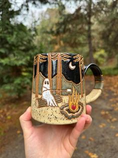 someone is holding up a ceramic mug with a dog in the woods on it's side