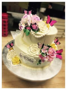 a three tiered cake with flowers and butterflies on it sitting on a wooden table