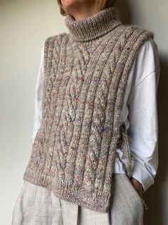 a woman standing next to a wall wearing a knitted sweater and vest with cables on it