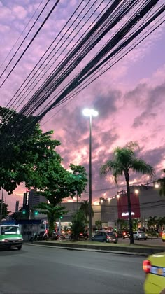 cars driving down the street at dusk with power lines in the air and palm trees