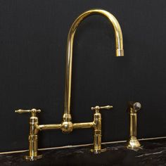 an antique brass sink with two faucets on the side and a black wall behind it