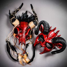 two red and black masks with horns attached to them on a gray surface, one has long hair