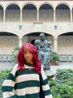 a woman with red hair standing in front of a statue wearing a green and white striped sweater