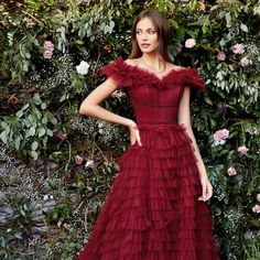 a woman standing in front of a bush wearing a red dress with ruffles