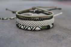 three different bracelets with green and white cords on concrete surface, close up view