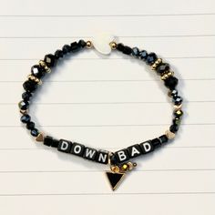 a black and gold beaded bracelet with the word down bad written on it's side