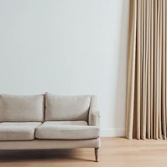 a white couch sitting in front of a window with drapes on the windowsill