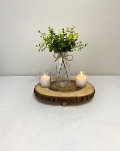 a glass vase with flowers and candles on a wooden tray