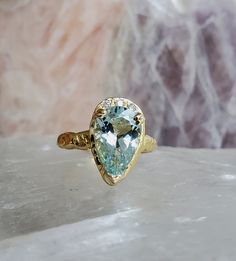 a gold ring with an aqua blue topazte in the center on a marble surface