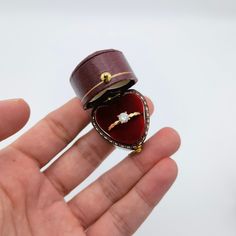 a hand holding a ring with a heart shaped box on it